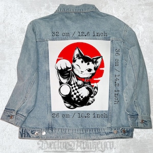 May include: Light blue denim jacket with a large graphic on the back. The graphic features a winking black and white cat in front of a red circle. The graphic measures 12.6 inches wide by 14.2 inches high and 10.2 inches long.