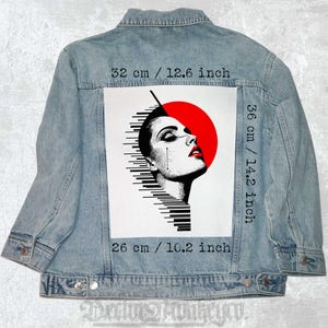 Könnte beinhalten: Ein weißer Patch mit einer schwarz-weißen Grafik eines Frauenkopfes mit einem roten Kreis hinter ihrem Kopf. Der Patch ist 36 cm hoch und 26 cm breit. Der Patch ist an einer hellblauen Jeansjacke befestigt.