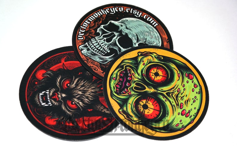 May include: Three round, black-edged patches with spooky illustrations. One features a skull, another a snarling wolf, and the third a zombie-like face. The top patch has the text "vectormonkeyco.etsy.com" in a circular design.