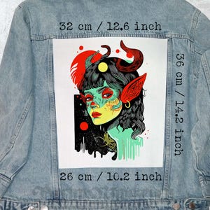Könnte beinhalten: Hellblaue Jeansjacke mit großem Grafikdruck auf dem Rücken. Die Grafik zeigt eine Frau mit roten Hörnern, Ohren und grüner Haut. Die Grafik misst 32 cm breit, 36 cm hoch und 26 cm lang. Klassischer Stil.