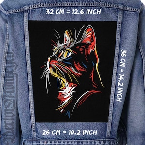 Peut inclure: Une veste en jean avec un patch noir représentant une illustration stylisée colorée d'une tête de chat. Le patch comporte des mesures en pouces et en centimètres. 32 CM = 12.6 INCH, 26 CM = 10.2 INCH, 36 CM = 14.2 INCH.