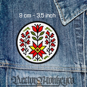 May include: A round patch with a floral design in red, yellow, green, and white, set against a black background. The patch is 3.5 inches in diameter and is displayed on a denim jacket.