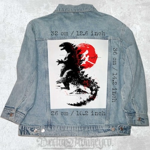 Op de afbeelding: Een zwart-witte illustratie van Godzilla die voor een rode zon staat met Japanse karakters. De illustratie is gedrukt op een witte patch, die is bevestigd aan een blauw denim jack. De patch is 32 cm breed en 36 cm hoog.