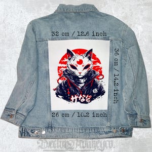 May include: Pale blue denim jacket with a striking graphic on the back. The graphic depicts a white cat mask with red details against a red sun. The graphic measures 32 cm wide, 36 cm tall, and 26 cm across.