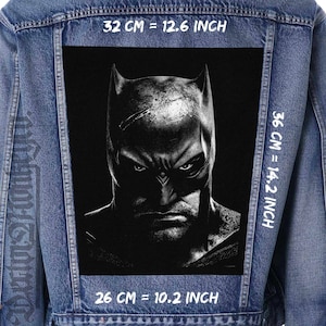 May include: A black and white image of Batman's face on a denim jacket. The image is 32 cm wide, 36 cm tall, and 26 cm deep. The measurements are also listed in inches.