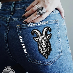 May include: A black and white goat head patch is ironed onto a blue denim jean pocket. The patch measures 8.5 cm by 13 cm. The text "Iron on Patch" is visible in the lower left corner.
