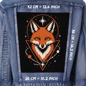 Könnte beinhalten: Eine blaue Jeansjacke mit einem großen rechteckigen Rückenaufnäher, der einen Fuchskopf in einem Dreieck und Kreis zeigt. Das Design enthält Sterne und Planeten. Der Text gibt Maße von 32 cm mal 36 cm mal 26 cm an.