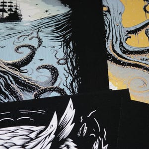K&ouml;nnte beinhalten: Eine Sammlung von Schwarz-Wei&szlig;-Kunstdrucken mit nautischen und Fantasy-Themen. Ein Druck zeigt ein Schiff auf See mit einem Oktopus, ein anderer einen Oktopus mit gelbem Hintergrund und ein dritter einen Wolf.