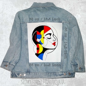 Könnte beinhalten: Eine Jeansjacke mit einem bunten abstrakten Kunst-Patch auf der Rückseite. Der Patch zeigt ein stilisiertes weibliches Gesicht mit geometrischen Formen in Rot, Blau, Gelb und Schwarz. Der Patch misst 36 cm x 26 cm.