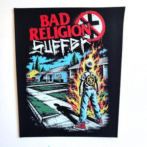 May include: A black fabric patch featuring the Bad Religion Suffer album artwork. It depicts a person standing in flames on a suburban sidewalk, with red text reading BAD RELIGION and white text reading SUFFER above a red crossbuster logo.