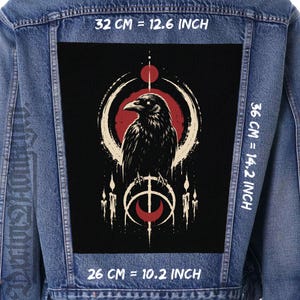 Può includere: Una giacca di jeans blu con una grande toppa rettangolare sul retro raffigurante un corvo nero, un sole rosso e motivi a mezzaluna bianchi. La toppa misura 32 cm per 36 cm, con una larghezza inferiore di 26 cm.
