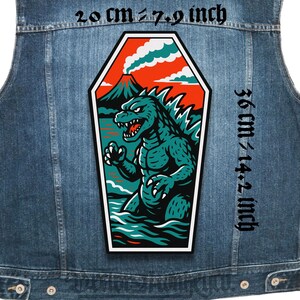 May include: A denim vest with a large, rectangular patch featuring a teal Godzilla-like monster emerging from water, with a volcano and red sky background. The patch measures 20 cm wide and 36 cm tall.