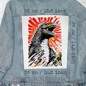 May include: Pale blue denim jacket with a large graphic on the back. The graphic is a black and white illustration of a monster with an open mouth against a red and orange background. The graphic measures 32 cm wide, 36 cm tall, and 26 cm long.