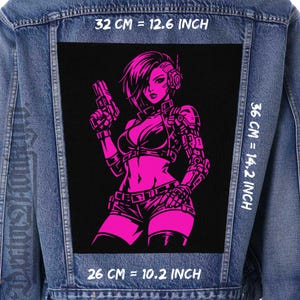 Peut inclure: Veste en jean avec un grand patch noir représentant une illustration rose d'une femme futuriste tenant une arme. Le patch mesure 32 cm par 36 cm et 26 cm. Le texte "32 CM = 12.6 INCH", "36 CM = 14.2 INCH", et "26 CM = 10.2 INCH" est visible.