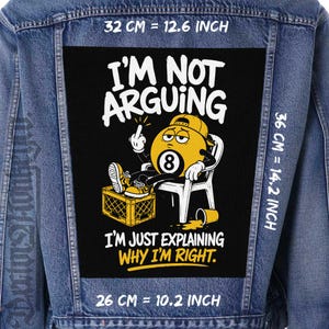 Puede incluir: Una chaqueta de mezclilla azul con un parche rectangular negro grande que muestra un personaje de bola 8 sentado en una silla, con el texto I'M NOT ARGUING I'M JUST EXPLAINING WHY I'M RIGHT. El parche mide 32 cm por 36 cm.