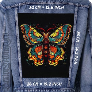 Puede incluir: Chaqueta vaquera azul con un parche de mariposa colorido. El parche, de 32 cm de ancho y 36 cm de alto, muestra una detallada ilustración de una mariposa en tonos naranja, amarillo, azul y verde sobre fondo negro.