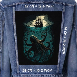Può includere: Una giacca di jeans nera con una toppa sul retro. La toppa presenta un'illustrazione in nero e verde scuro di un kraken che attacca una nave. Il testo "32 CM = 12.6 INCH", "36 CM = 14.2 INCH" e "26 CM = 10.2 INCH" è stampato sulla giacca.