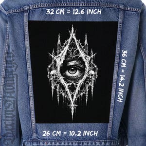 Könnte beinhalten: Eine blaue Jeansjacke mit einem großen, rechteckigen schwarzen Aufnäher auf dem Rücken, der ein weißes Motiv eines menschlichen Auges zeigt, eingerahmt von gotischen Architekturelementen und zwei Totenköpfen. Der Aufnäher misst 32 cm mal 36 cm.