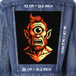 Peut inclure: Veste en jean avec un grand écusson rectangulaire représentant un cyclope de dessin animé avec des détails orange et jaune sur fond noir. L'écusson mesure 32 cm sur 36 cm.