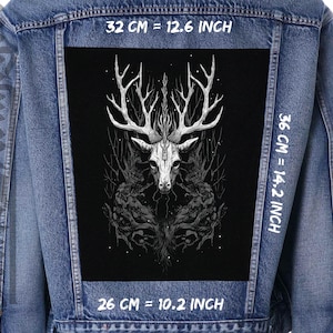 Puede incluir: Una chaqueta vaquera negra con un parche negro en la espalda que presenta un gráfico blanco de una calavera de ciervo con cuernos en un entorno de bosque. El parche mide 32 cm de ancho por 36 cm de alto. El texto "32 CM = 12.6 INCH", "36 CM = 14.2 INCH" y "26 CM = 10.2 INCH" está impreso en la chaqueta.