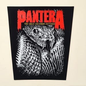 May include: A black rectangular fabric patch featuring a red Pantera logo at the top with the text The Great Southern Outtakes in yellow below it. The centre displays a detailed white graphic of a snake head with fangs and a forked tongue.