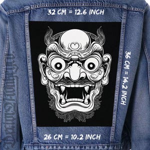 Peut inclure: Veste en jean avec un grand patch noir représentant une illustration blanche détaillée d'un masque de démon japonais. Le patch mesure 32 cm de large, 36 cm de haut et 26 cm de long.