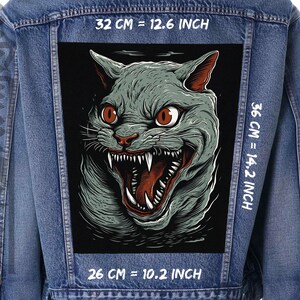 Peut inclure: Une illustration en noir et blanc d'un chat grognant avec des yeux rouges. L'image est imprimée sur une veste en jean avec du texte blanc qui indique "32 CM = 12.6 INCH", "36 CM = 14.2 INCH" et "26 CM = 10.2 INCH".