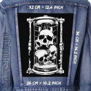 Pode incluir: Jaqueta jeans com um grande patch preto com uma ilustração branca detalhada de caveiras dentro de uma ampulheta. O patch mede 32 cm de largura, 36 cm de altura e 26 cm de comprimento.