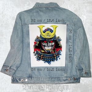 Peut inclure: Veste en jean bleu clair avec un grand motif de samouraï dans le dos. Le motif représente un guerrier avec un casque et un sourire menaçant. Le motif mesure 32 cm de large et 36 cm de haut.