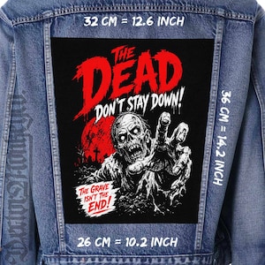 Könnte beinhalten: Eine blaue Jeansjacke mit einem großen rechteckigen schwarzen Aufnäher auf der Rückseite. Der Aufnäher zeigt eine Zombie-Grafik mit rotem Text THE DEAD DON'T STAY DOWN! und THE GRAVE ISN'T THE END! Die Maße betragen 32 cm mal 36 cm.