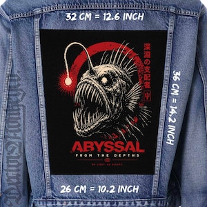 Peut inclure: Une veste en jean bleu avec un grand écusson rectangulaire au dos. L'écusson présente une illustration de baudroie avec des accents rouges, du texte japonais et les mots ABYSSAL FROM THE DEPTHS. Les dimensions sont 32 cm par 36 cm par 26 cm.