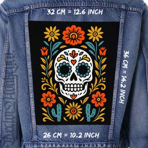 May include: A denim jacket with a large, rectangular patch featuring a sugar skull design. The patch is black with a white skull, surrounded by orange, yellow, and blue floral elements. The patch measures 10.2 inches by 14.2 inches.
