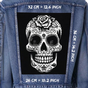 May include: A black denim jacket with a white sugar skull patch on the back. The patch is 12.6 inches wide and 14.2 inches tall. The skull is decorated with intricate floral designs and a rose.