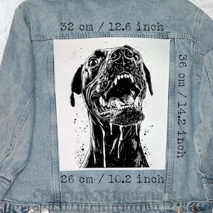May include: Light blue denim jacket featuring a large black and white graphic of a snarling dog. The graphic measures 12.6 inches wide, 14.2 inches high, and 10.2 inches long. The jacket is a classic style with a button-up front and pockets.