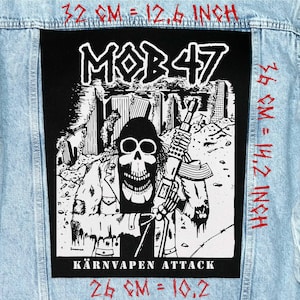 Puede incluir: Un parche en blanco y negro con el texto "MOB47" y "KÄRNVAPEN ATTACK". El parche presenta una calavera sosteniendo un rifle, con dimensiones de 32 cm por 36 cm y 26 cm. El parche está sobre una chaqueta vaquera azul claro.