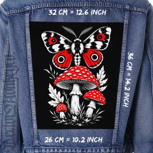 Può includere: Una giacca di jeans blu con una grande toppa rettangolare sul retro. La toppa presenta uno sfondo nero con una falena bianca e rossa sopra tre funghi rossi e bianchi. Il testo indica dimensioni di 32 cm per 36 cm.