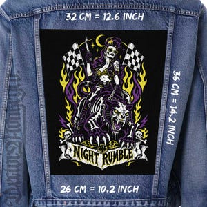 Pode incluir: Um casaco de ganga azul com um grande emblema retangular nas costas, apresentando uma pessoa montada numa pantera esquelética. O design inclui bandeiras axadrezadas, chamas amarelas e o texto NIGHT RUMBLE. Mede 32 cm por 36 cm.