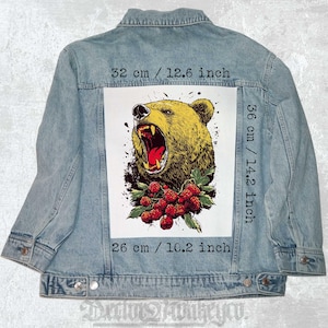 Op de afbeelding: Een spijkerjack met een grote strijkbare patch met een brullende bruine beer met rode bessen. De patch is 36 cm bij 26 cm.