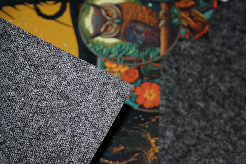 May include: A section of a decorative rug featuring a detailed owl illustration. The owl is brown and orange, set against a backdrop of colorful flowers and foliage. A gray, textured fabric is in the foreground.