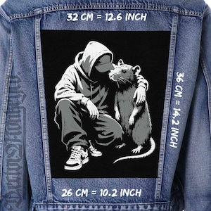 May include: A blue denim jacket featuring a large black and white rectangular patch on the back. The patch depicts a hooded figure crouching beside a large rat. Text on the image indicates dimensions of 32 cm by 26 cm width and 36 cm height.