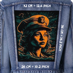 Puede incluir: Un parche bordado negro y naranja con una mujer que lleva una gorra azul marino con un emblema dorado. La mujer tiene el pelo oscuro y mira hacia la derecha. El fondo es una escena oceánica azul oscuro y verde. El parche mide 32 cm de ancho, 36 cm de alto y 26 cm de profundidad.