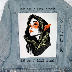 Puede incluir: Chaqueta vaquera azul claro con un gran estampado rectangular. El estampado presenta una ilustración estilizada de una mujer con detalles en naranja, cabello negro y una capucha. Mide 32 cm de ancho, 36 cm de alto y 26 cm de largo.