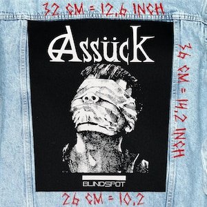 May include: A light blue denim jacket with a large black patch featuring the word "Assück" in white, above a black and white illustration of a person with a bandage over their eyes. The text "BLINDSPOT" is below the illustration. The patch measures 12.6 inches by 14.2 inches.
