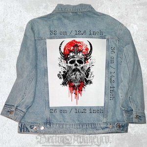 Puede incluir: Un parche blanco para planchar con una ilustración en blanco y negro de una calavera con una corona y cuernos. La calavera tiene barba y gotea sangre roja. El fondo es un círculo rojo con un contorno blanco. El parche mide 26 cm por 36 cm.