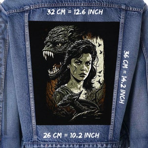 Peut inclure: Une veste en jean noire avec un patch au dos. Le patch représente une femme aux longs cheveux noirs et une créature aux dents acérées. Le texte sur le patch indique "32 CM = 12.6 INCH", "36 CM = 14.2 INCH" et "26 CM = 10.2 INCH".