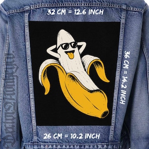 May include: A blue denim jacket featuring a large rectangular patch on the back. The patch displays a yellow and white banana character wearing black sunglasses with its tongue out. Text indicates dimensions of 32 cm by 36 cm and 26 cm by 36 cm.