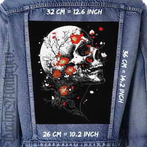 Puede incluir: Un cráneo blanco y negro con flores rojas y flores blancas sobre un fondo negro. El cráneo está rodeado por un círculo blanco con un contorno negro. La imagen está en una chaqueta vaquera con medidas en pulgadas y centímetros.