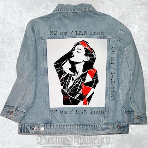 Peut inclure: Veste en jean bleu clair avec un motif graphique d'une femme en noir, blanc et rouge. Le motif mesure 32 cm de large, 36 cm de haut et 26 cm en bas. La veste a un design classique avec des boutons et des poches.