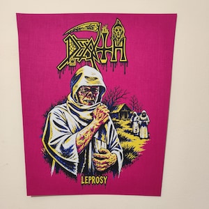 Pode incluir: Um emblema de tecido retangular com um fundo magenta vibrante e uma ilustração gráfica de uma figura encapuzada com lesões cutâneas visíveis. O texto DEATH aparece no topo com uma fonte estilizada e a palavra LEPROSY está impressa abaixo.