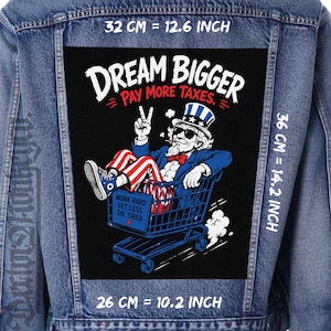 Könnte beinhalten: Eine blaue Jeansjacke mit einem großen rechteckigen Rückenaufnäher, der Uncle Sam in einem Einkaufswagen zeigt. Der Text lautet DREAM BIGGER PAY MORE TAXES und WORK HARD GET LESS DIE TIRED. Der Aufnäher misst 32 cm mal 36 cm in der Größe.